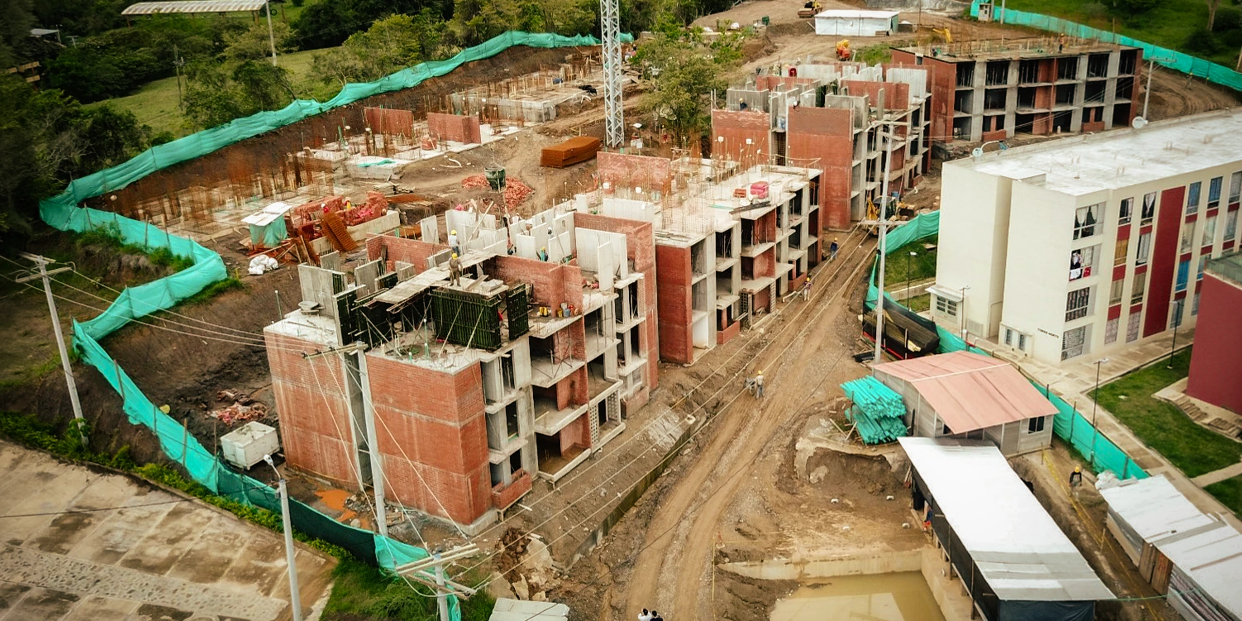 La obra desde el aire: los muros de concreto fundidos en sitio avanzan por etapas ladera abajo, junto a los primeros bloques terminados.